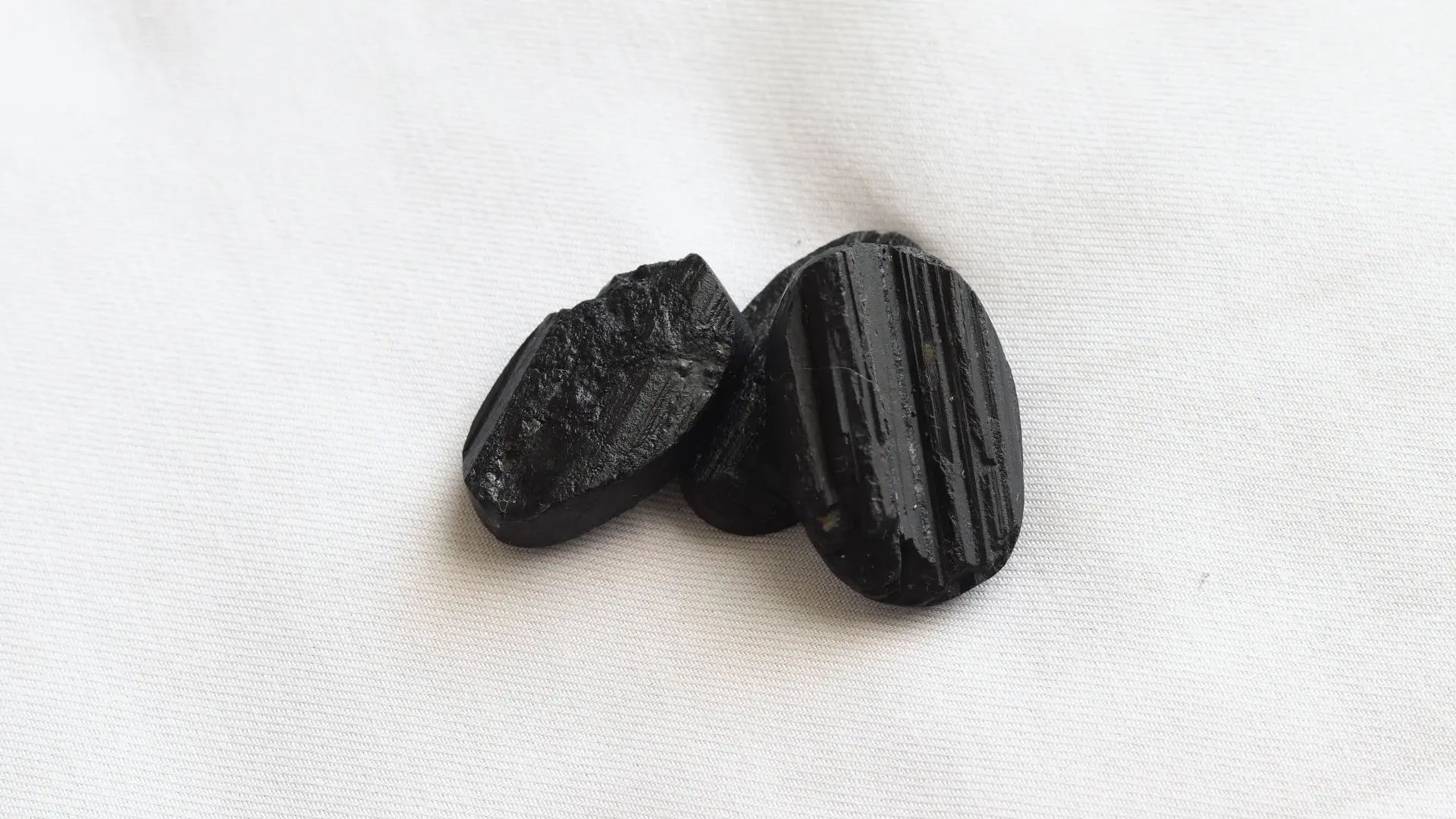 Three pieces of raw black tourmaline, with deep grooves along the crystal, on white fabric
