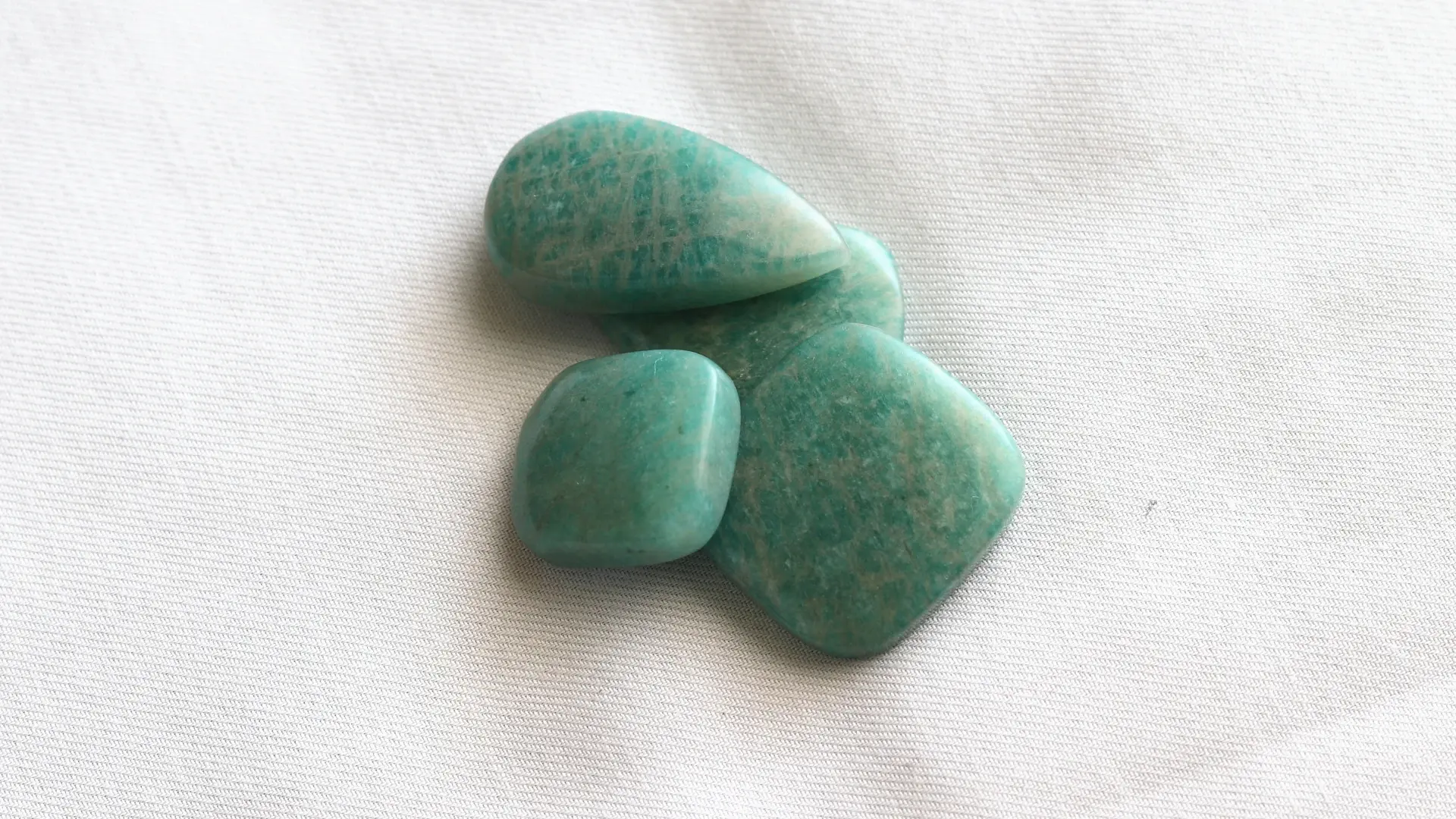 Four polished turquoise-green amazonite stones with pale streaks, on white fabric